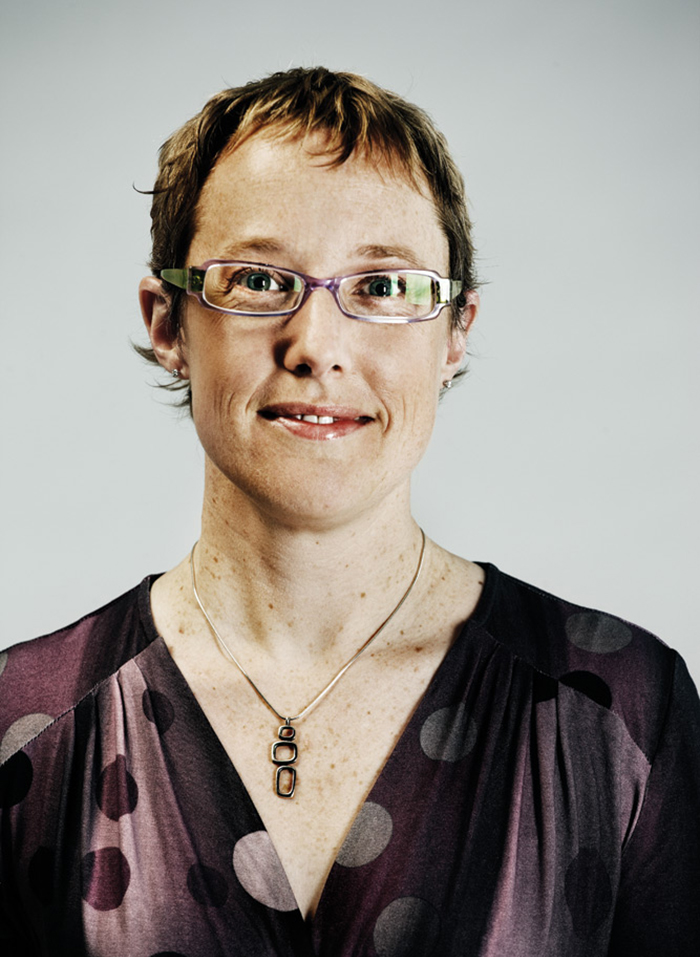 Headshot of Breese Davies, wearing light purple-framed glasses and a light and dark purple blouse with polka dots
