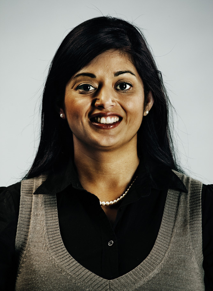 Headshot of Gurjit Sangha, wearing a black collared shirt, light grey knit tank top, and pearl earrings and necklace