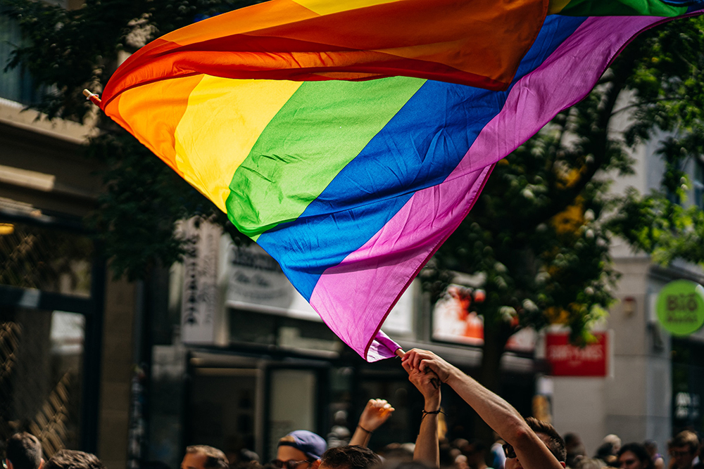 Close up of pride flag being waved by a person among a group of people on a street