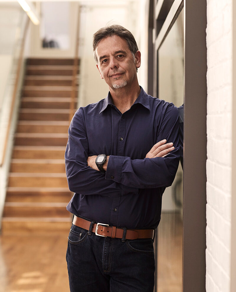 Indoor photo of Professor Ron Deibert, leaning against a glass surface with arms crossed