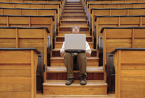 Photo of a person sitting on wood stairs behind a laptop.