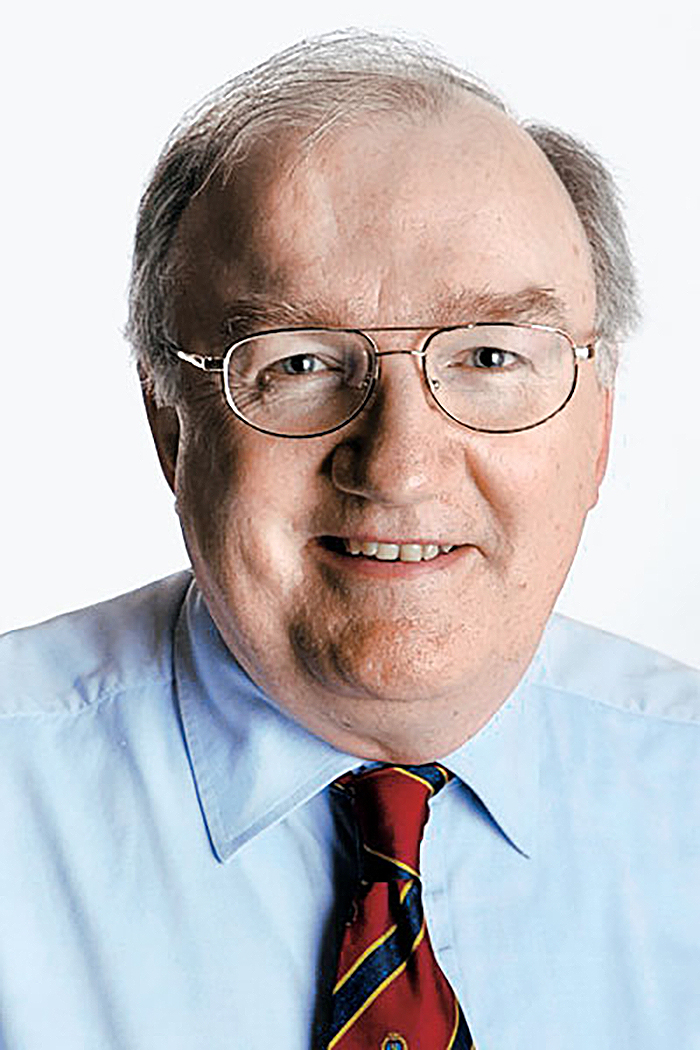 Headshot of Michael Walsh in black wire-rimmed glasses, a blue collared shirt and a blue-striped red tie
