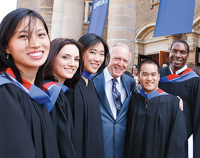 Terrence Donnelly in front of Convocation Hall, standing next to graduating students in convocation gowns, all smiling at the camera