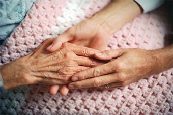 Photo of a woman's hands holding an elderly woman's hand.