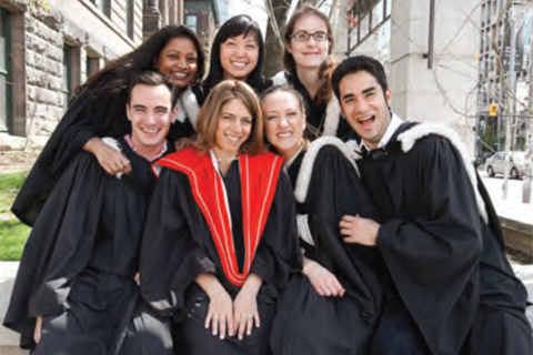 A group of new graduates in convocation robes posing for a photo by U of T's front campus