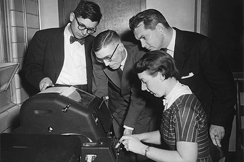Professor Calvin Gotlieb (with bow tie) and CN Telegraph officials look on as programmer Audrey Bates makes computer history.
