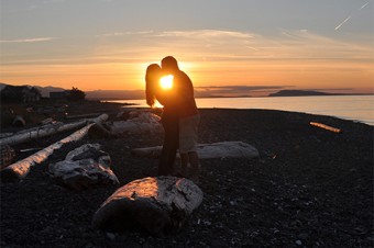 Two figures kiss in front of a sunset.