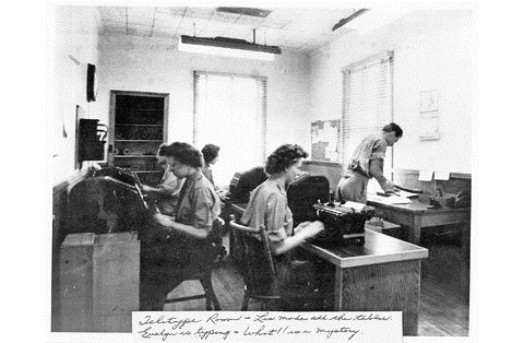 Black and white photo of a room of workers typing on mechanical typewriters