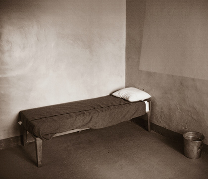 A b&w photo of a single bed in a room.