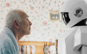 A elderly man and a robot look at one another.
