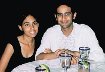 Cynthia Jairam-Persaud, in a black short-sleeved top, and Anil Persaud, in a white button-up long-sleeved shirt, dressed up, seated at a round table with drinks in front of them