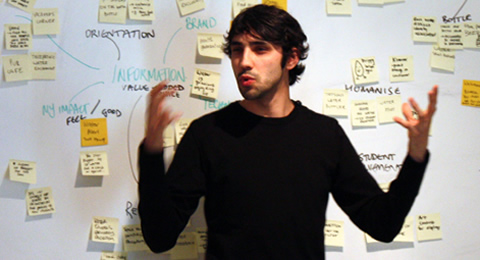 Photo of a man giving a speech in front of an idea board.