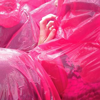Photo of a hand poking out from under a pile of red-pink plastic bags