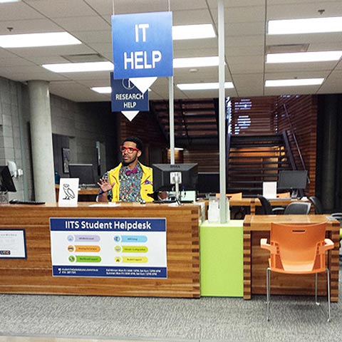 Photo of Drake behind the IITS Student Helpdesk, wearing red glasses