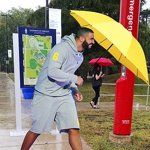 Photo of Drake walking on UTSC grounds, holding a yellow umbrella
