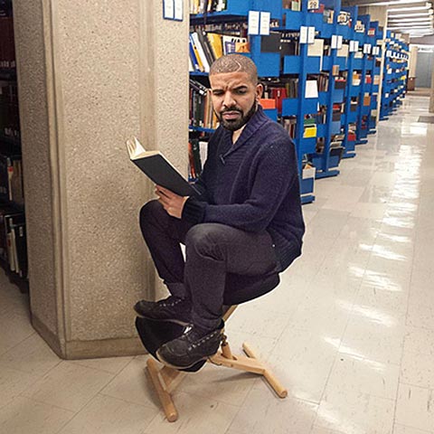 Photo of Drake reading a book among the UTSC library stacks