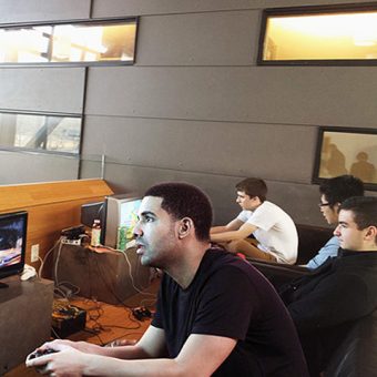 Photo of Drake sitting at a student lounge, playing video games