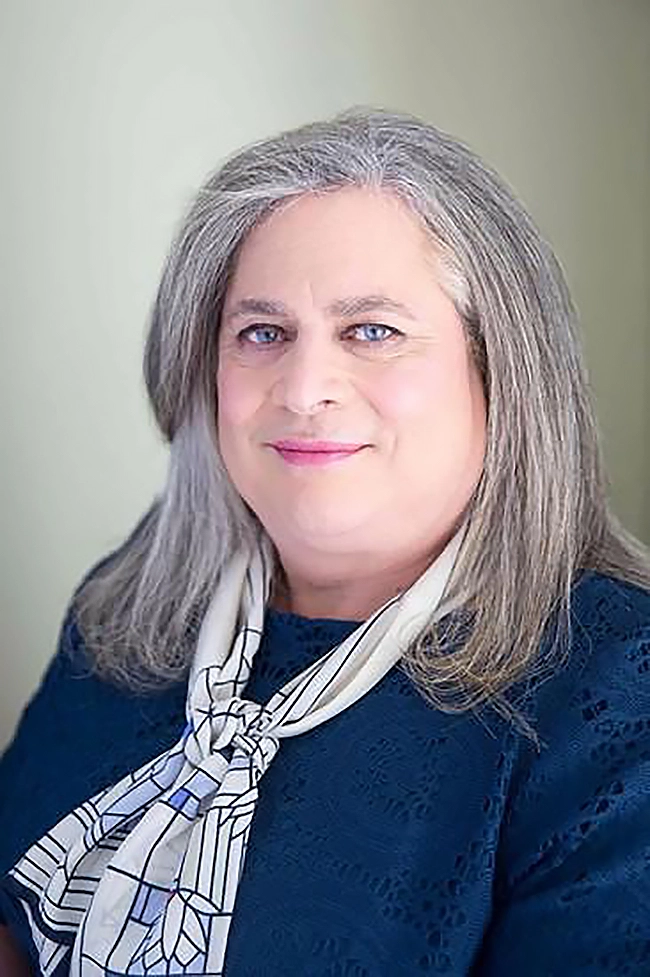 Studio headshot of Jennifer Pritzker wearing a blue sweater and a white and blue kerchief around her neck