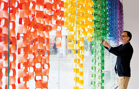 Photo of Trevor Young adding paper loops to the Faculty of Medicine's Display Your Pride installation