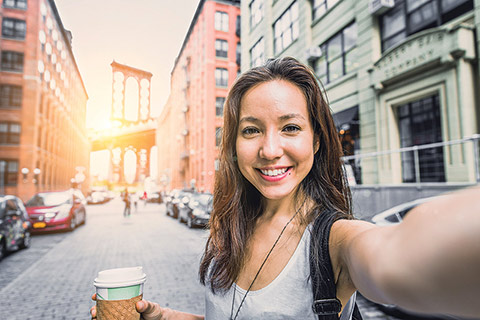 Selfie photo of a woman holding a coffee cup in the middle of a street
