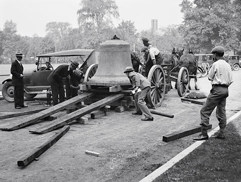 Photo of workers unloading a large bell from a horse-drawn wagon