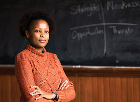 Photo of Sylvia Mwangi in front of a classroom chalkboard