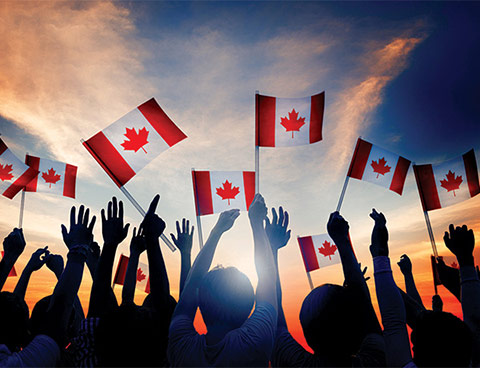 Sunset shot of hands in the air, waving Canadian flags