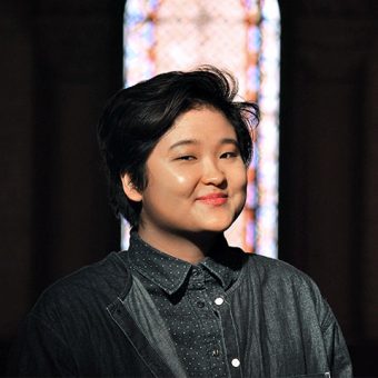 Head shot of Celeste Yim in a dark space in front of stained glass window
