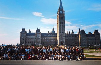 Photo of 100 female U of T students in front of a building on Parliament Hill.