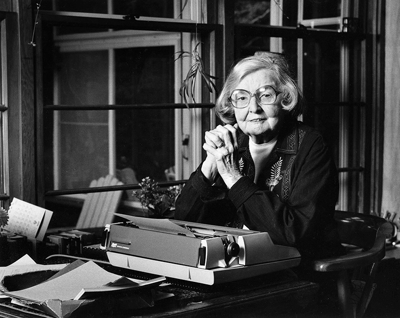 Black and white photo of Edna Staebler at her desk, a typewriter in front of her.