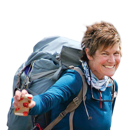 Photo of a smiling Alison Wiley carrying a large backpack and holding out a cellphone.