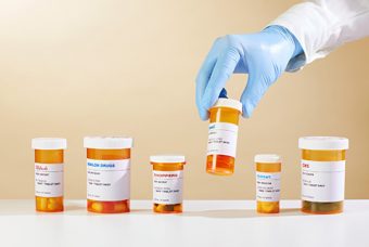 Photo of a plastic-gloved hand picking up the fourth of six prescription medicine containers in a row.