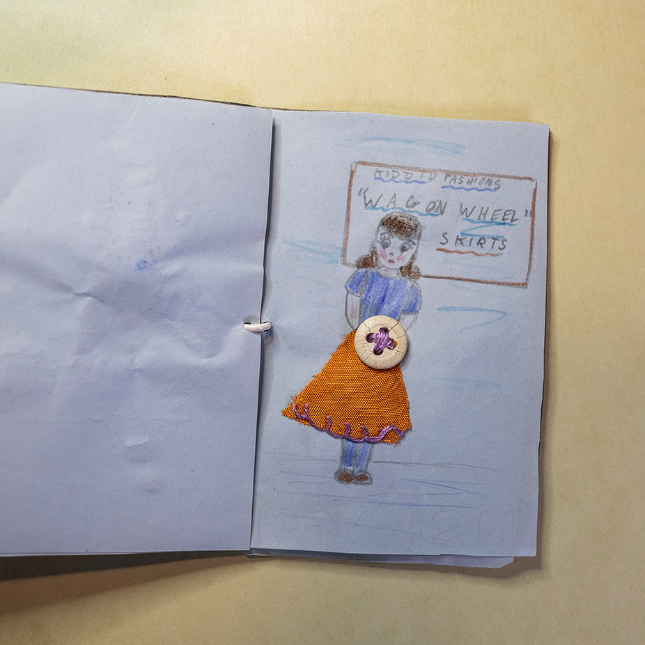 Open handmade book showing a drawing of a girl with a belt made of a button sewn into the drawing