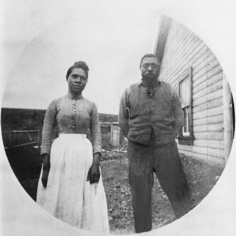 A black-and-white portrait of Mildred and John Ware, circa 1898, in front of their cabin