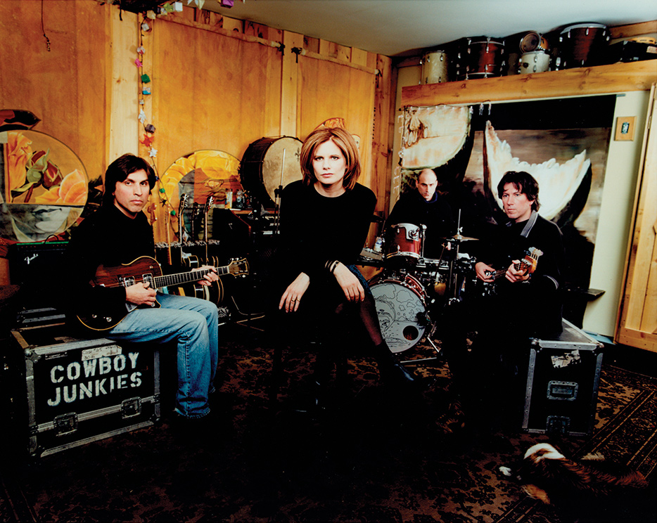 Group photo of Cowboy Junkies' Michael Timmins, Peter Timmins and Alan Anton sitting with their instruments, with Margo Timmins seated front and centre