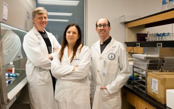 Ian McGilvray, Sonya MacParland, and Gary Bader in lab coats. Photo taken in a lab.