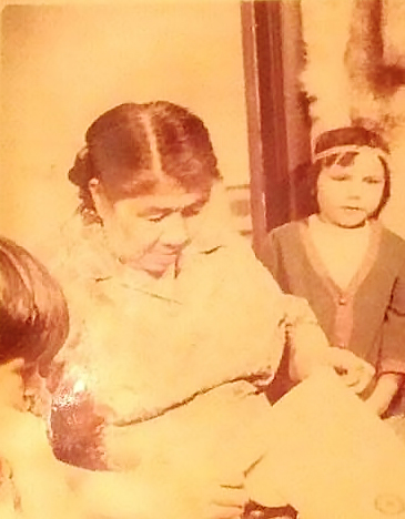 Sepia-toned photo of an older woman sewing, with a young girl wearing a headband to the right and Brenda Wastasecoot as the little girl on the left watching the woman's hands