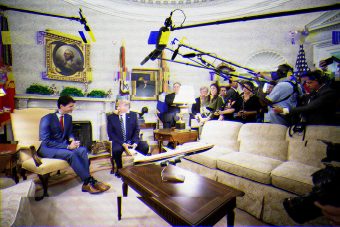 Staticky TV screen image of Prime Minister Justin Trudeau and President Donald Trump in armchairs on the left and a group of reporters watching them from behind a couch