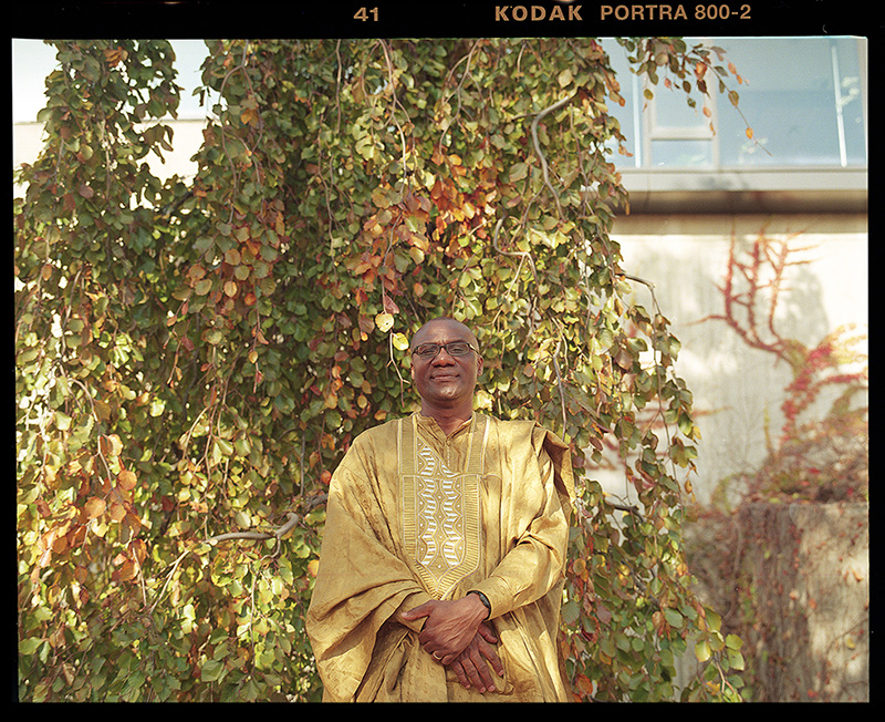 U of T Scarborough Principal Wisdom Tettey standing in front of vines of leaves by the side of a building.
