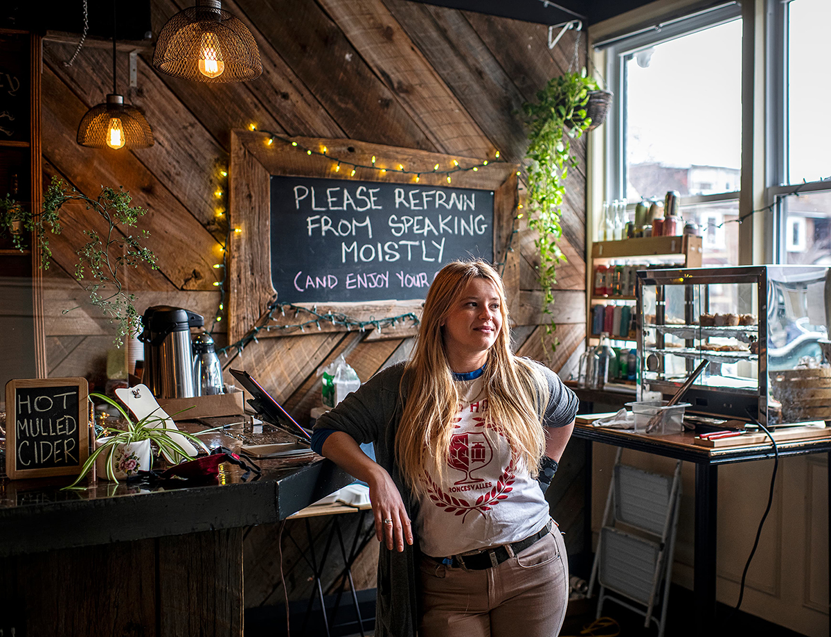 Sasha Steinberg inside Cider House, posing with her arm on the bar counter in front of a chalkboard sign reading 