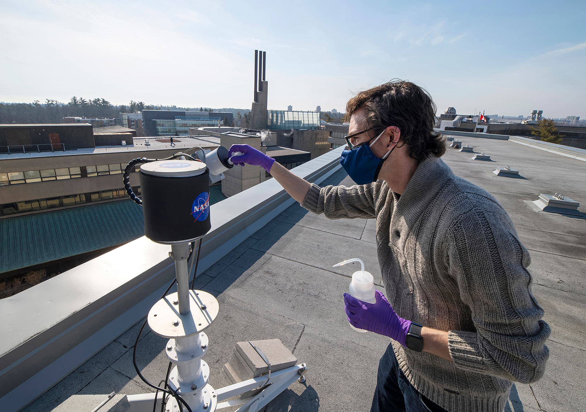 A researcher taking readings from the Pandora Spectrometer System on a rooftop