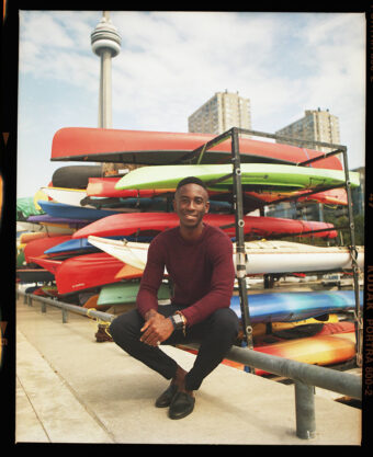 Ernest Nyarko in front of a rack of canoes and kayaks with the CN Tower in the background