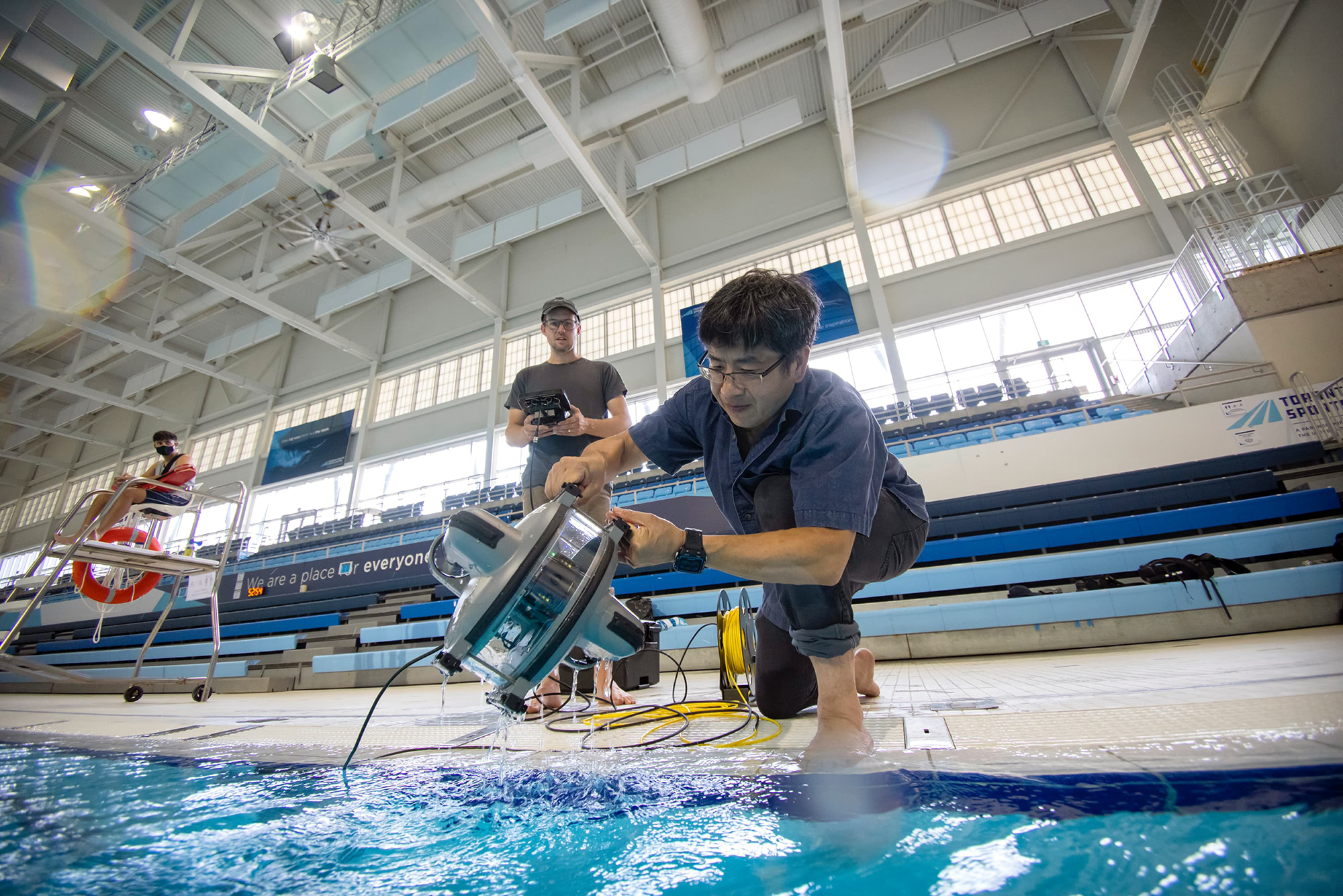 Chai Chen taking the underwater drone out of a pool, and Tom Meulendyk holding the controller