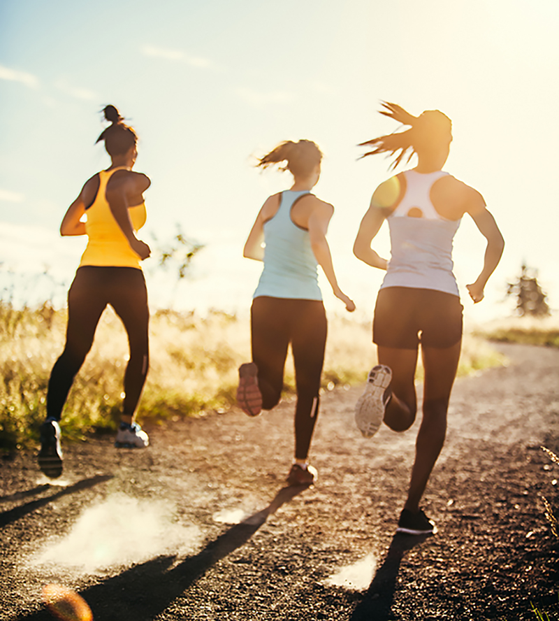 Three runners running on a dirt road in the sunlight