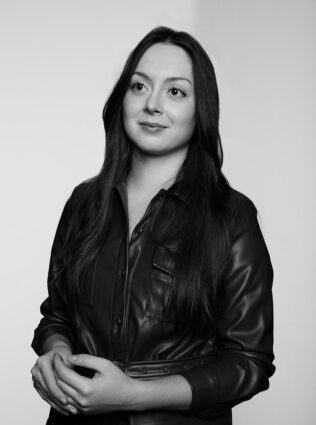 Black and white studio closeup of Emma McCann, wearing a black leather jacket, looking off camera