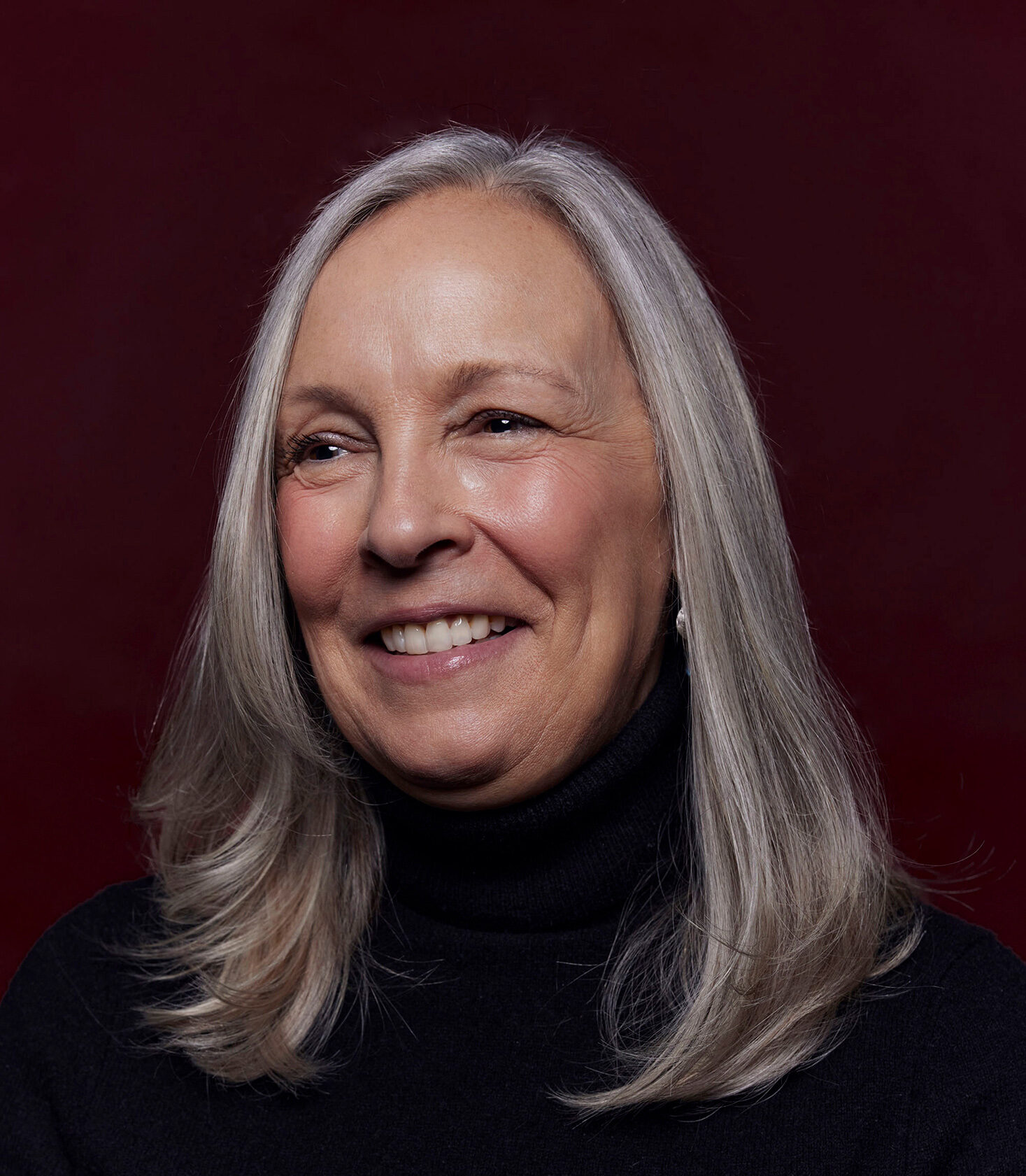 Close up of Prof. Gillian Hadfield in a black turtleneck sweater, smiling against a solid dark-brown background