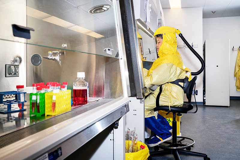 Jessica Lam wearing a yellow hazmat suit, conducting research in a lab