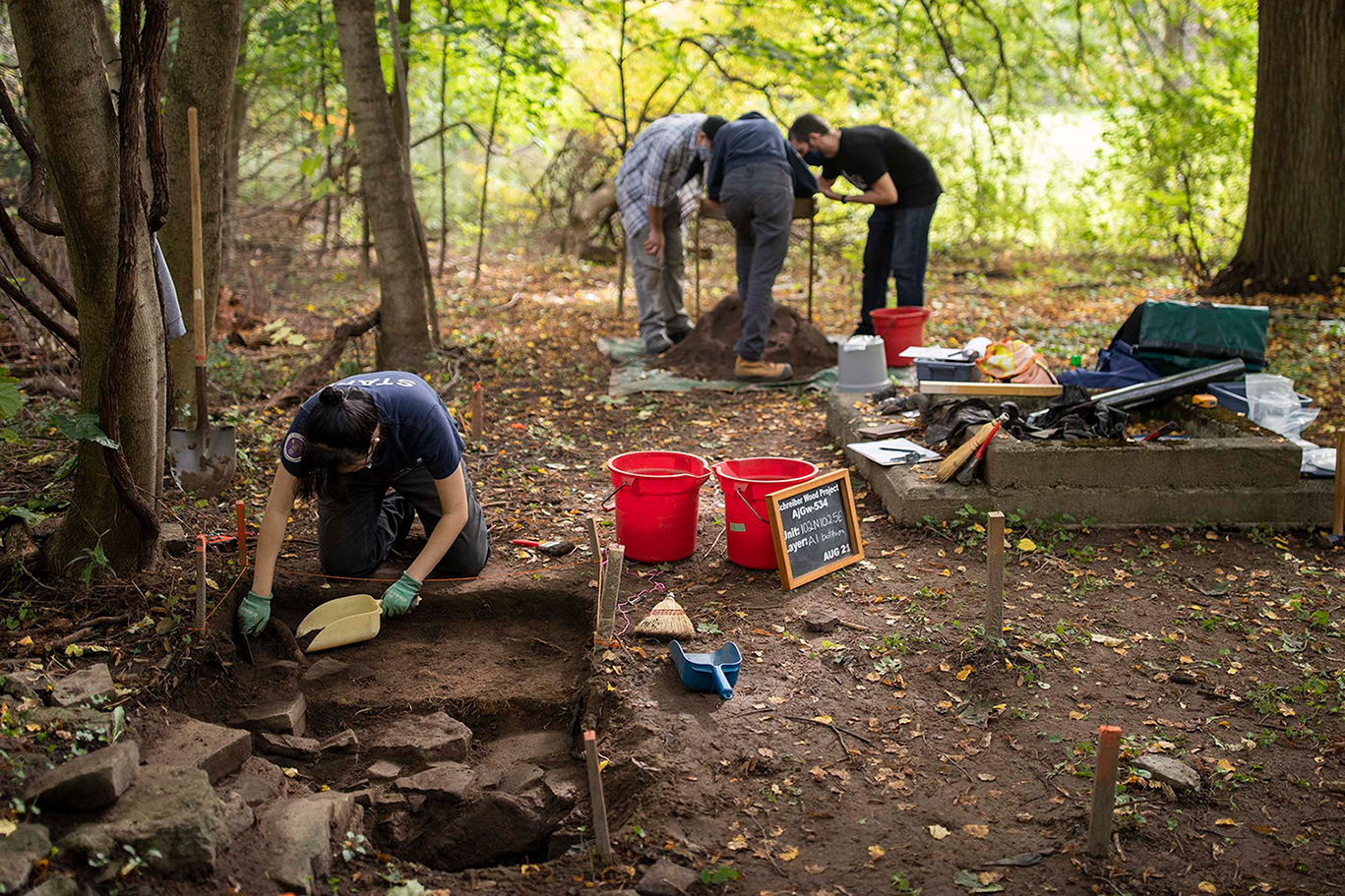 Student in the foreground digging in a sectioned off area, three students in the background examining a pile of dirt