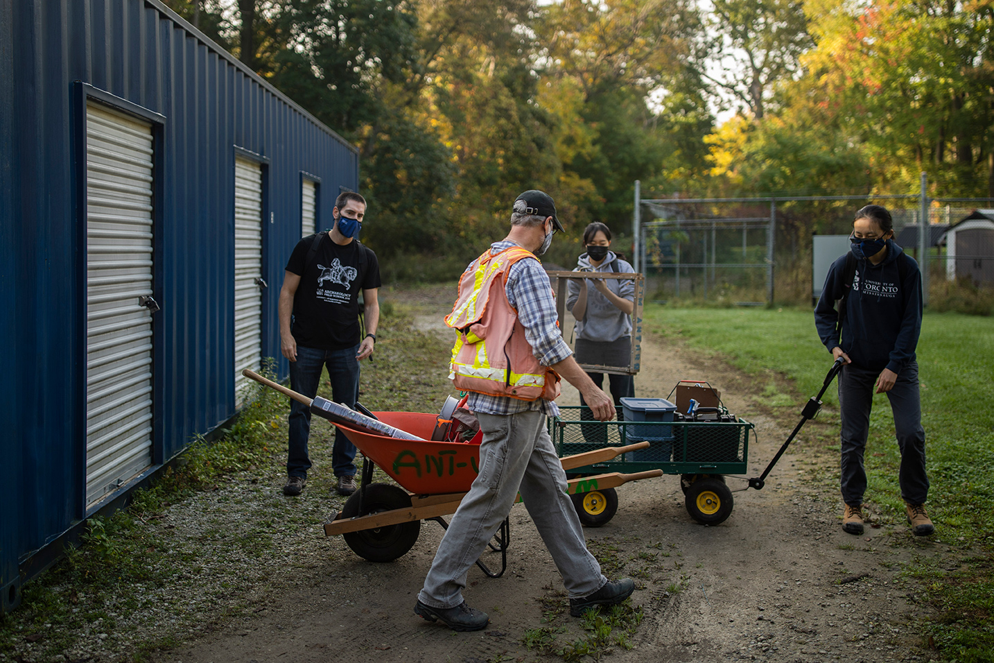 Students towing a wheelbarrow and carrying equipment