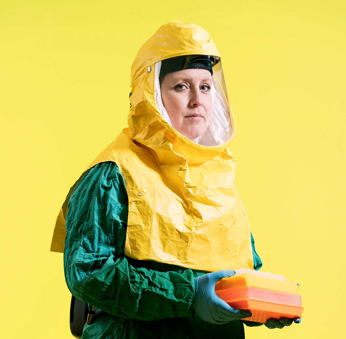 Researcher wearing a yellow and green hazmat suit, holding rectangular containers